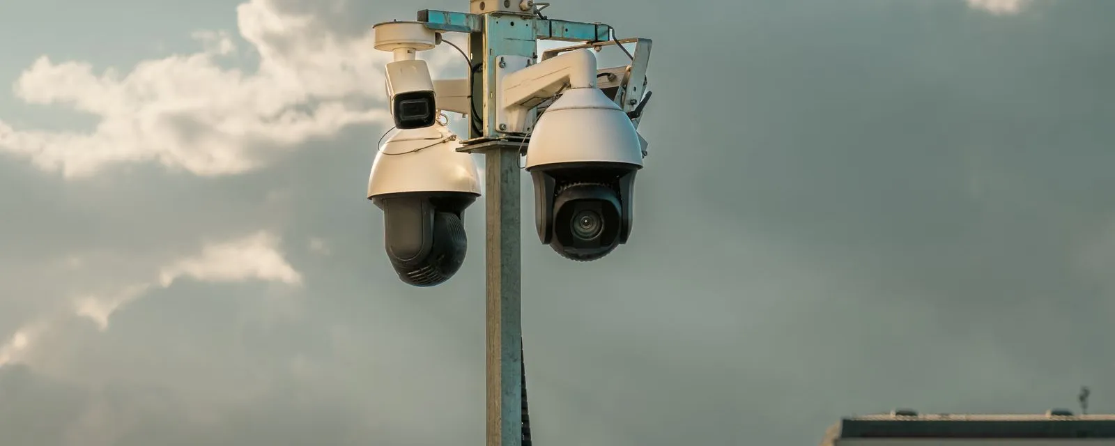 Bewakingscamera's hoog boven de daken, tegen een bewolkte lucht