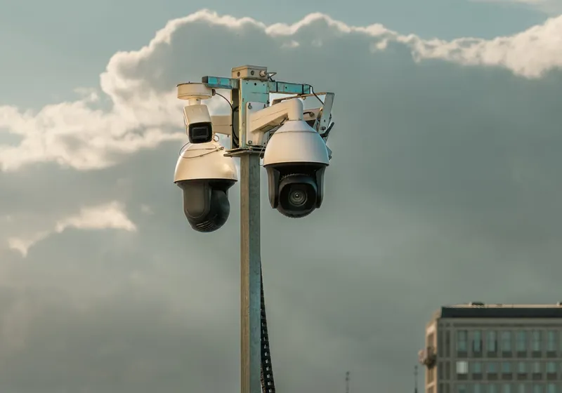 Twee bewakingscamera's op een mast, afgetekend tegen een bewolkte lucht